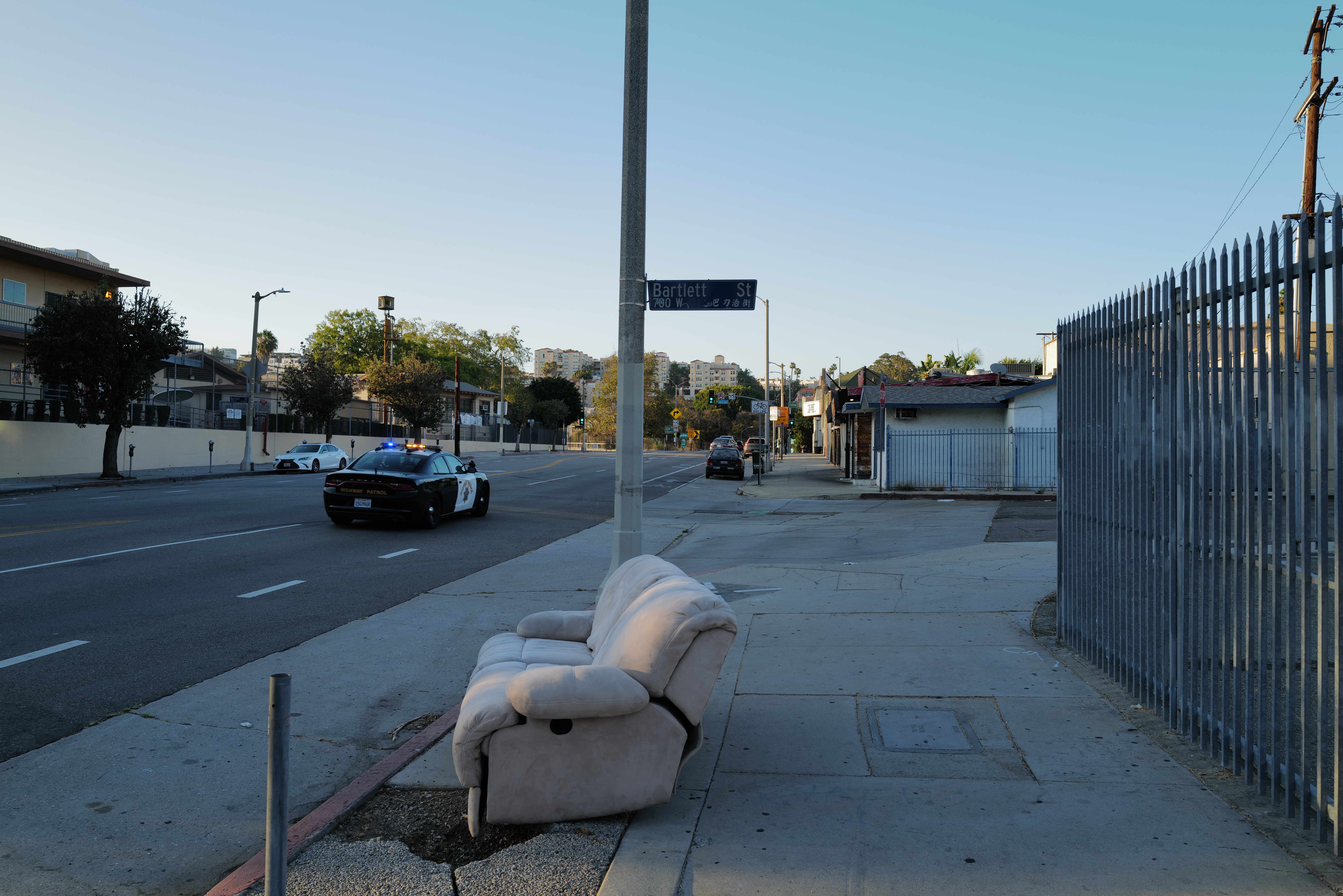 An abandoned reclining chair beside a Los Angeles street as a patrol car passes.